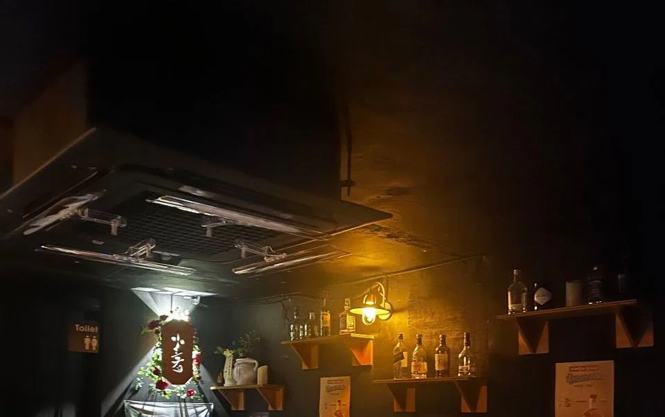 オレンジ色の壁灯がともる済州アホプ梨泰院店の店内。棚に酒瓶が並び、筆文字の看板が掛かっている